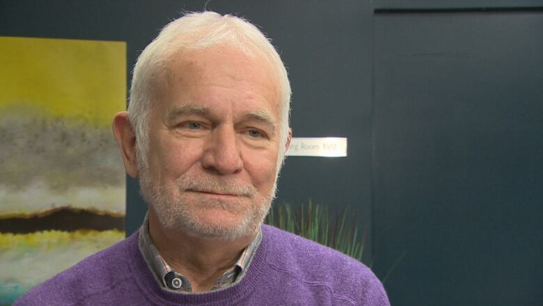 A man in a purple sweater, on top of his collared shirt, looks ahead.