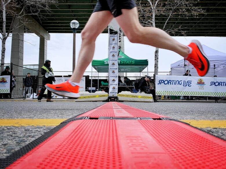 A runner in orange Nike shoes crosses a red finish line with a sporting life sign in the background.