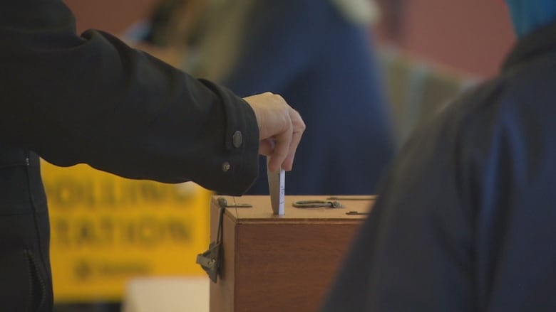 A hand holding a ballot ticket and putting it in a box