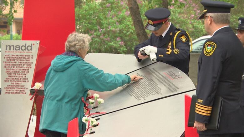 A woman puts her finger on a name at a sundial-shaped monument.