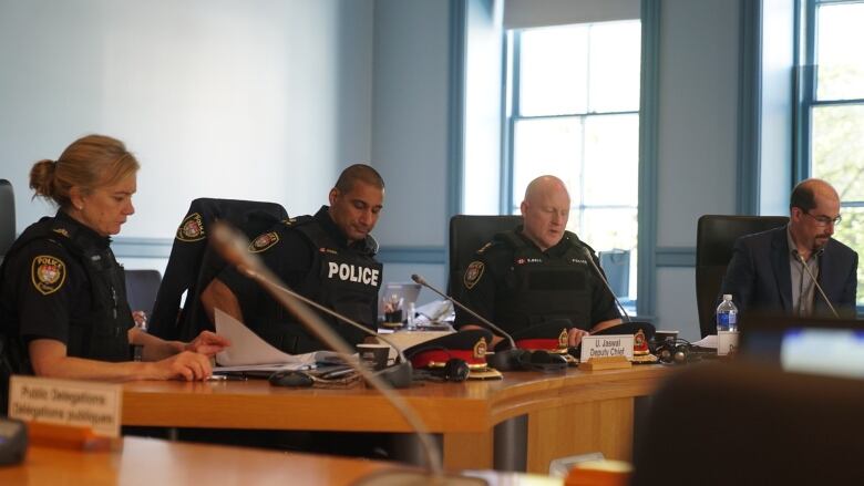 Four people, three in police uniforms, sit at a meeting table.