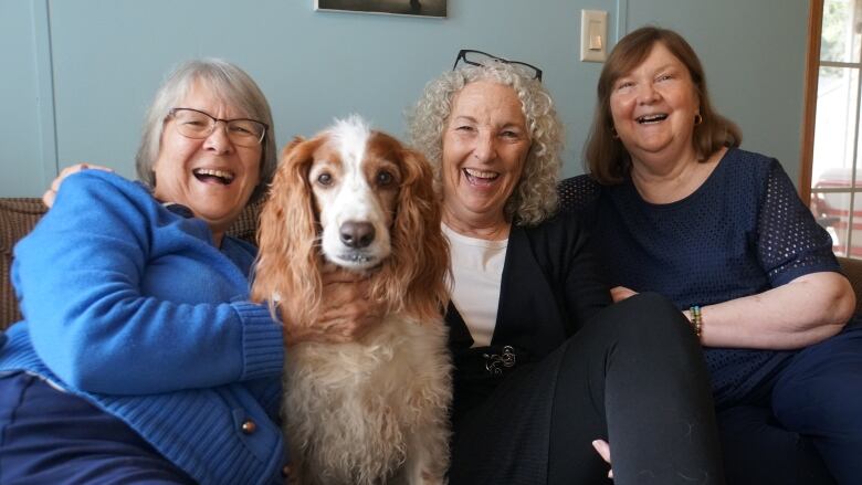 Three senior women pose with a golden retriever on the couch