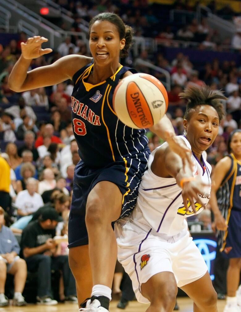 Two women's basketball players pursue a loose ball during a game.