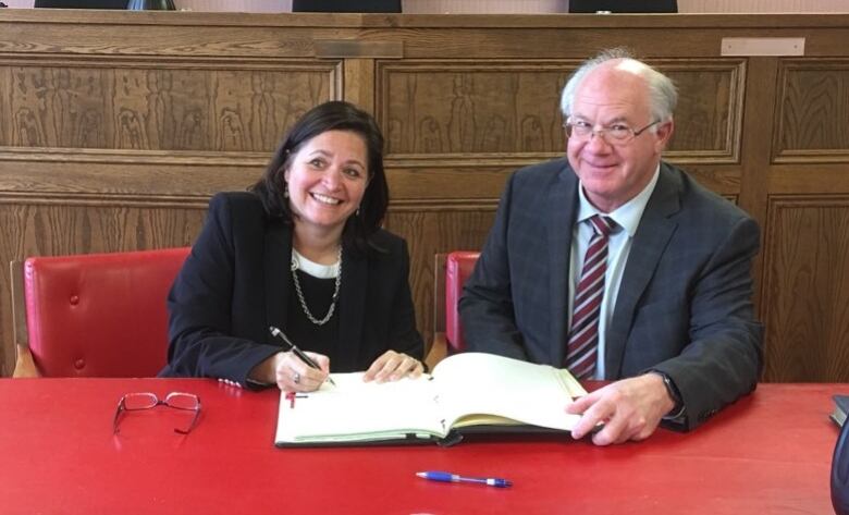 A woman and man seated at a red table with the woman signing an open book.