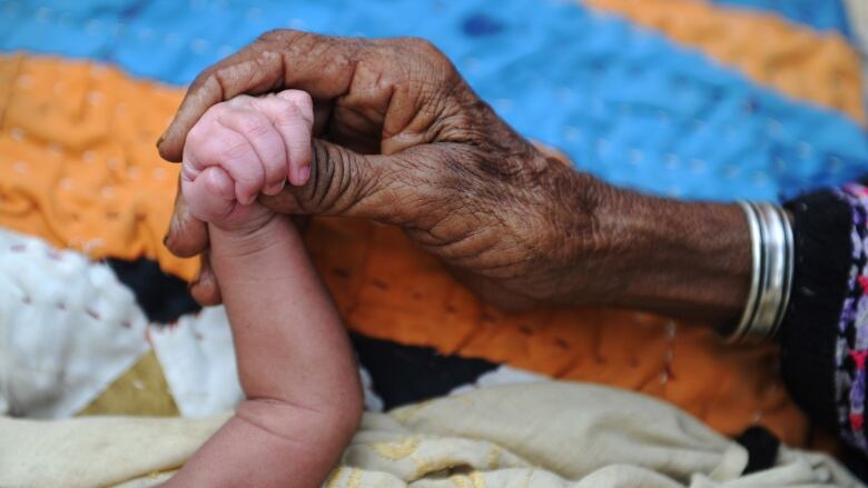 A grandmother holds the hand of their three-day-old grandchild.