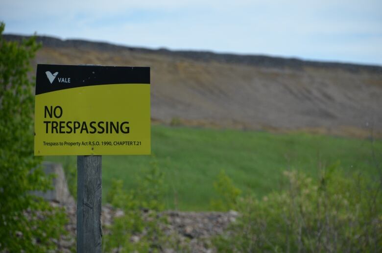 A no trespassing sign in front of a green hill.