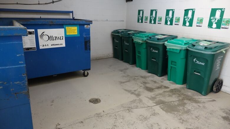 A room with a row of green bins and large blue recycling bins