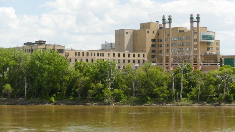 A hospital is pictured on the banks of a river, alongside green vegetation including trees.