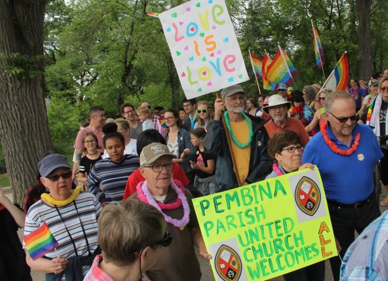 People walk in a Pride parade while carrying signs. 