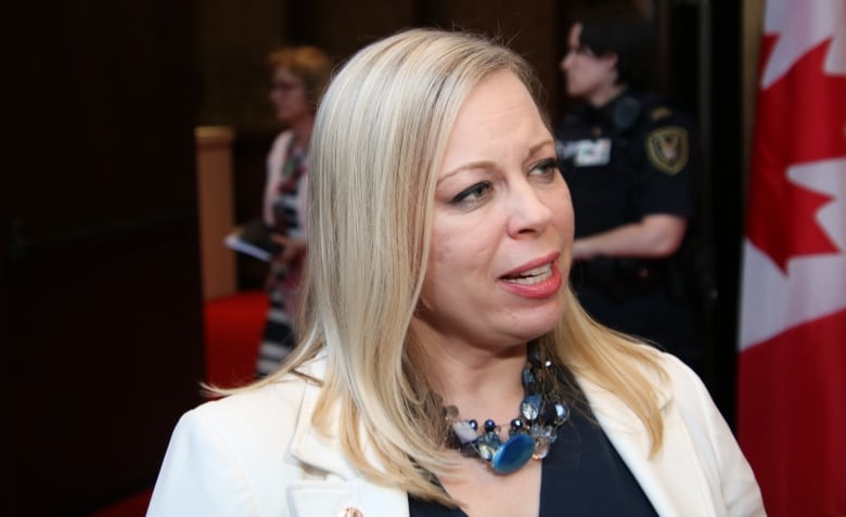 A woman speaks with a Canadian flag in the background.