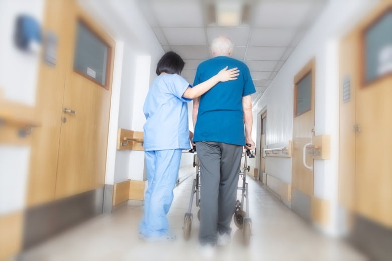 A care worker assists an elderly resident using a walker.