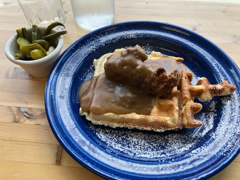 A plate containing a waffle topped with a piece of fried chicken and gravy.