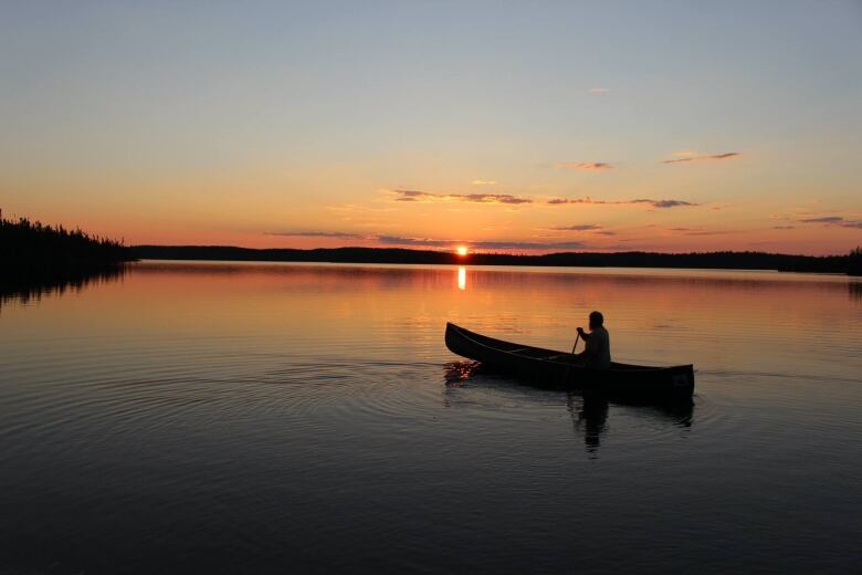 An image showing the silhouette of a canoe on the water with a vibrant sunset in the background. 