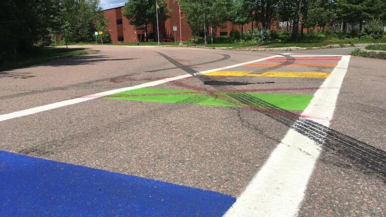 tire marks cover a rainbow crosswalk on a city road