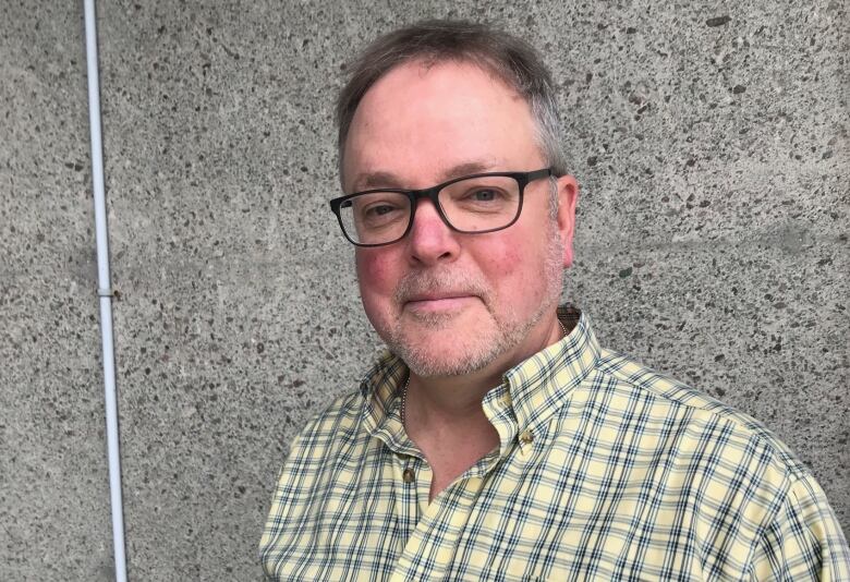 A man in a yellow checkered shirt smiles. 