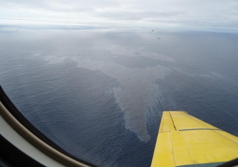 A panoramic photo of the Altantic Ocean through a plane window. A noticeable dark sheen of oil sits on top of the water.