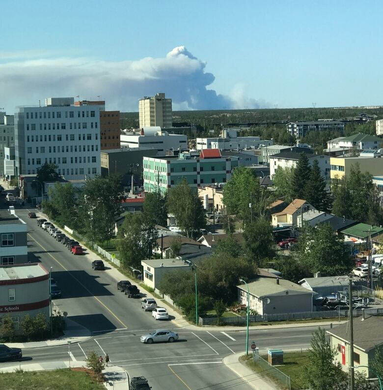 A plum of wildfire smoke is seen in the distance. Yellowknife buildings are visible in the foreground.