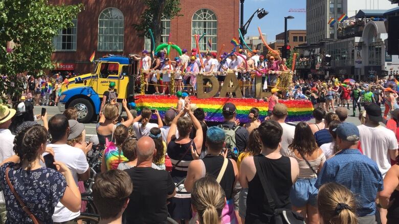 Many people are watching as a Pride parade float with people on it goes by.