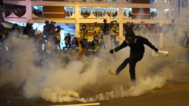 Protester kicks canister with smoke billowing out.