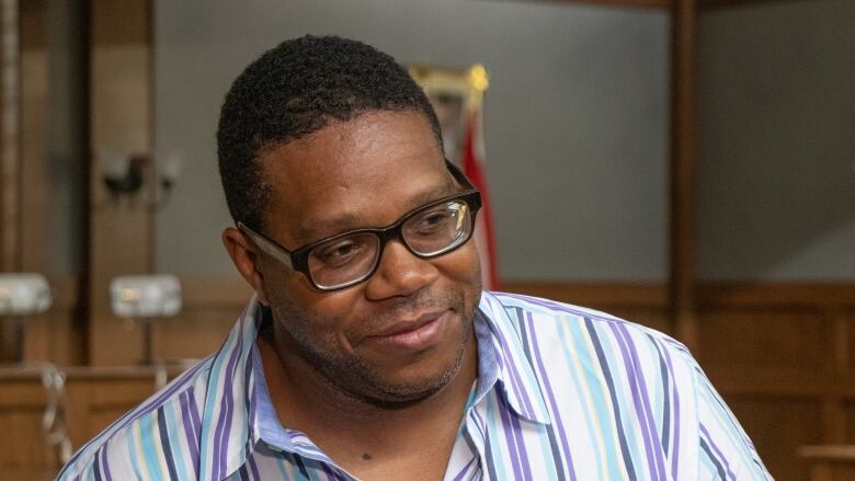 A Black man wearing glasses and a blue and purple stripped shirt