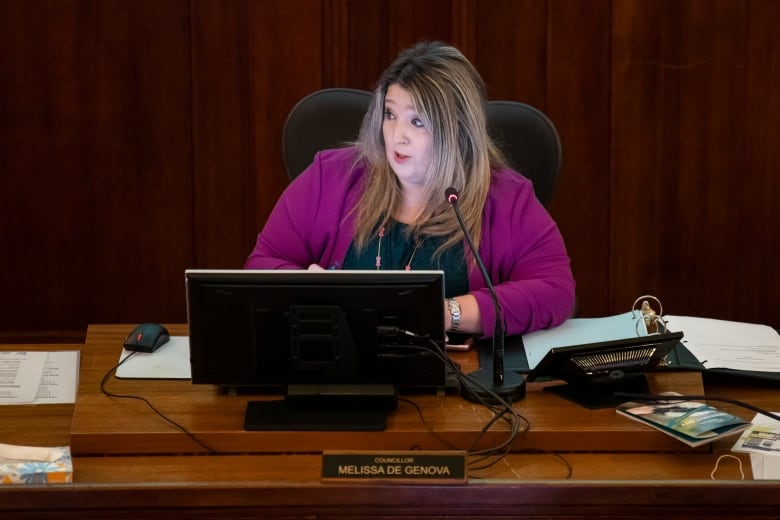 A white woman wearing a purple top speaks in council chambers.