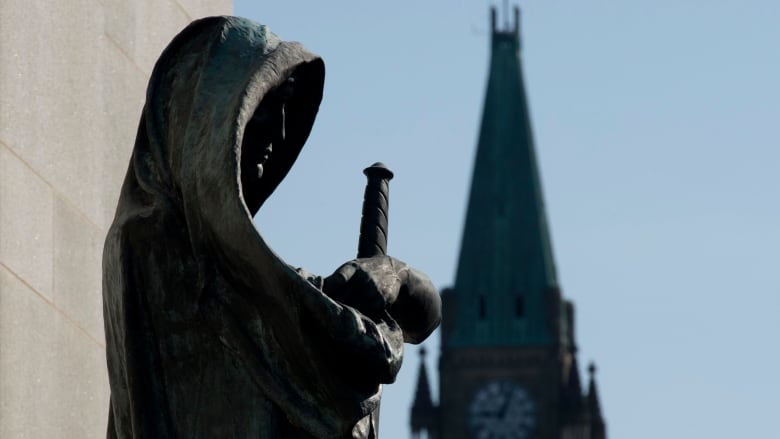 A statue holding a sword stands in front of a clocktower in Ottawa.