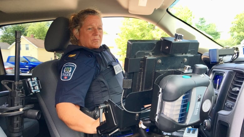 Police officer sitting in a police cruiser, looking at computer screen attached to central console.