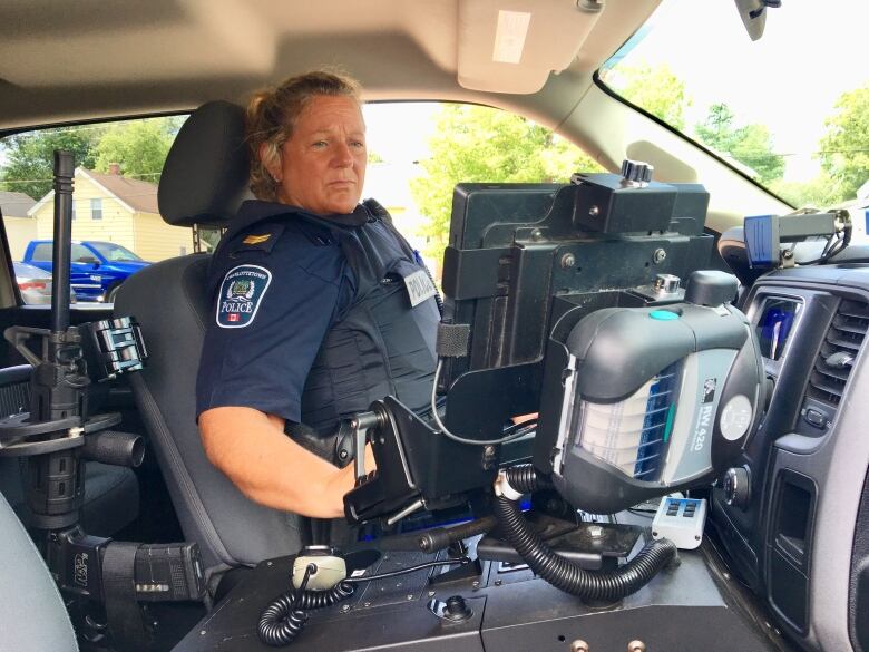 Police officer sitting in a police cruiser, looking at computer screen attached to central console.