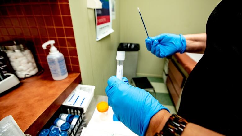 A person wearing blue medical gloves holds up a swab and a tube.