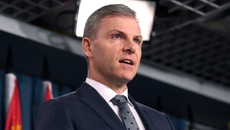 A man in a suit gestures with his hands as he speaks.