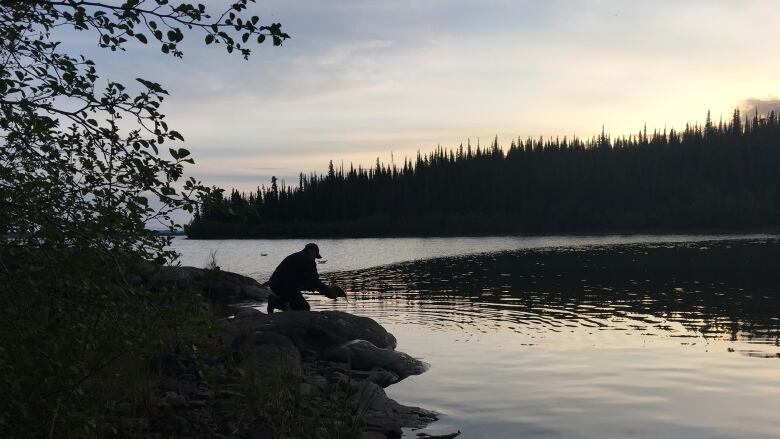 A man stands by a waters edge with a fish.