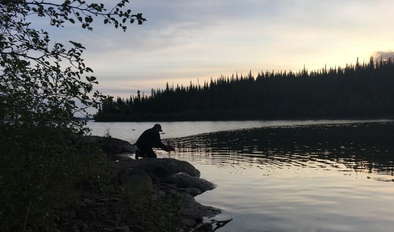 A man stands by a waters edge with a fish.