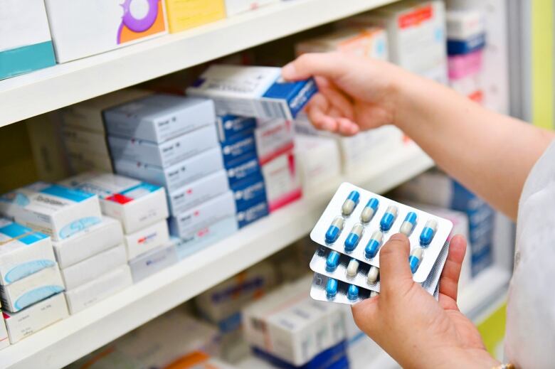 A pair of hands is shown stocking medications on a shelf in a pharmacy.