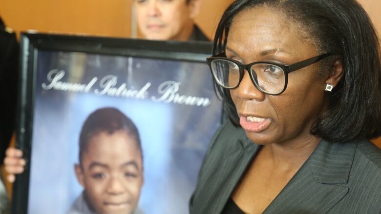 A woman speaking. There's a photo of a young child behind her that reads 