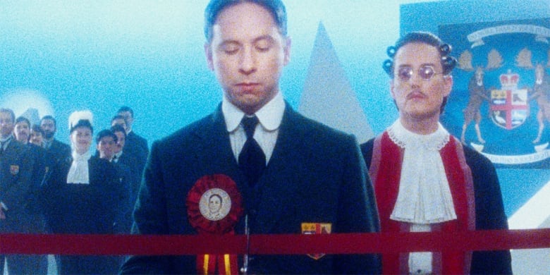 A dream-like still from a still shows a man in a suit, with others behind him.