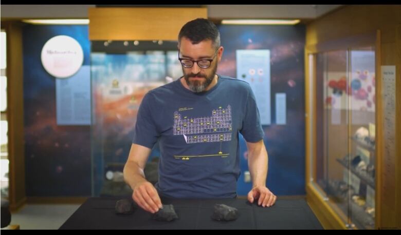 Man in periodic table t-shirt examines rocks on a table