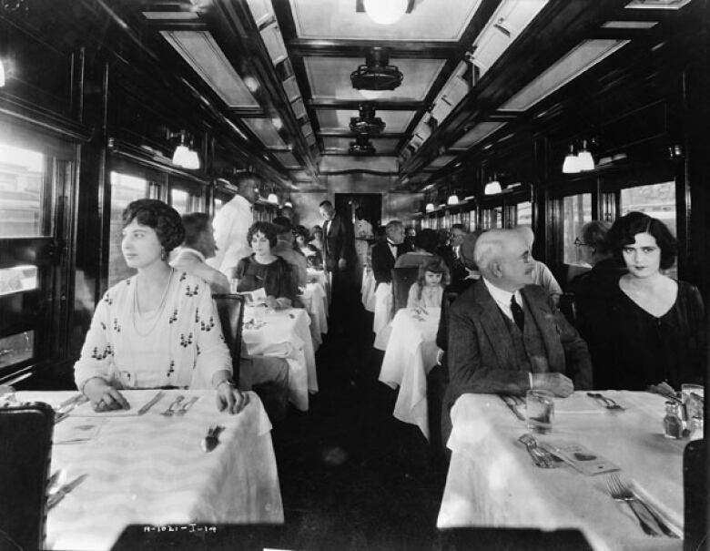 A black and white photo of people riding in the interior of a train.