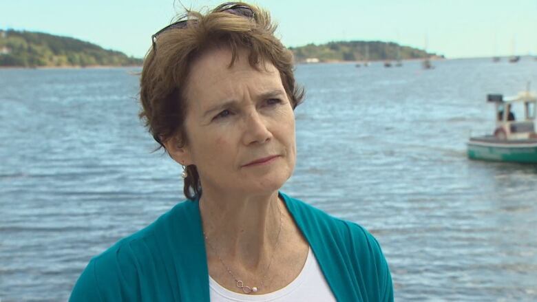 A white woman with short brown hair stands in front of the blue harbour with boats in the background