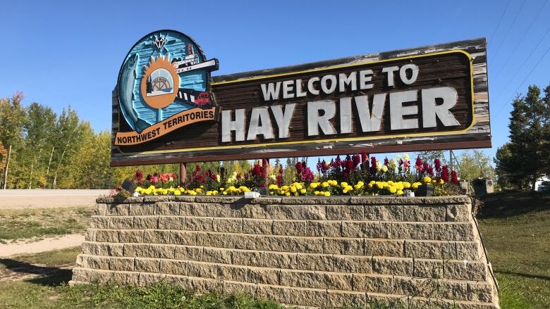 A sign that says Welcome to Hay River sits on top of rocks with trees in the background.