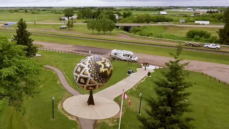 A brightly coloured oversized pysanka can be seen on the edge of a road passing by.