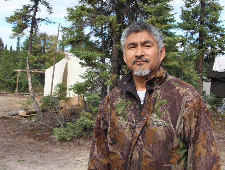 A man in a camo jacket sits in front of two white tents.