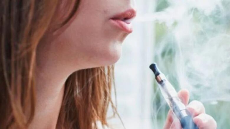 A young person holds a vape pen.