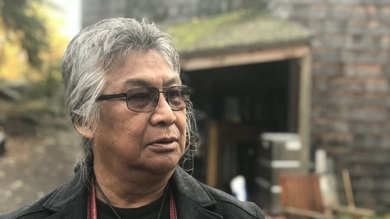 Portrait of a man with grey hair and glasses, standing outside.