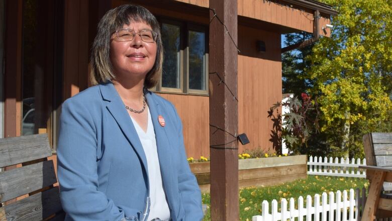 Woman posing for photo while grinning in front of a wooden home