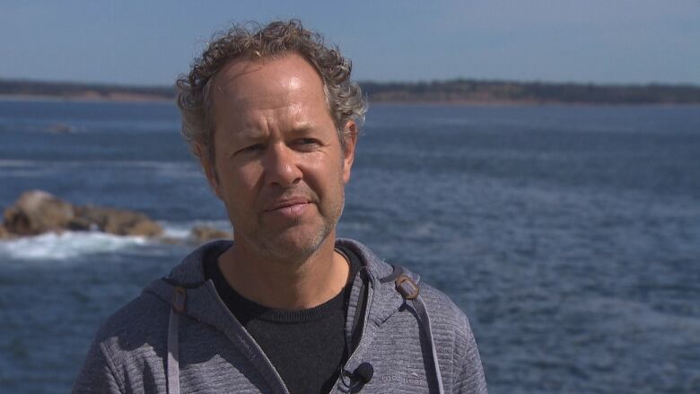 A man wearing a sweater standing in front of a ocean cove.