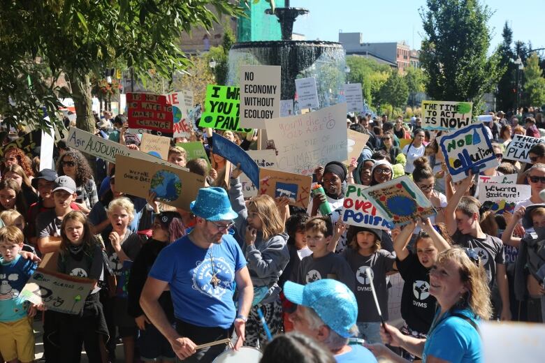 Many people gather together outdoors hold signs about the climate. They are in front of the Gore Park fountain.