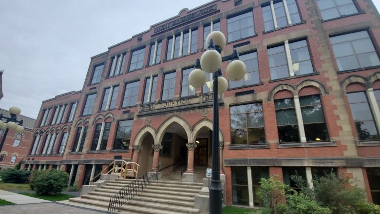 A brick building with the words Justice engraved at the top is shown, in front of a lamppost.