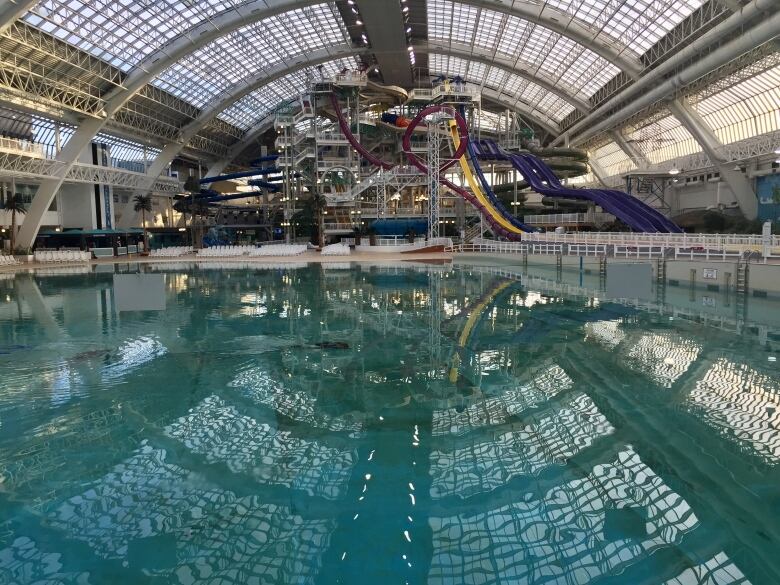 A view of a large pool with several waterslides in the background, beneath a glass ceiling.