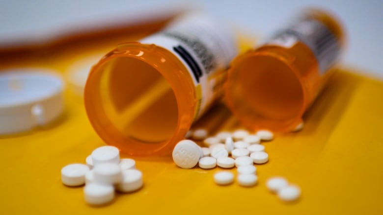 Two plastic bottles of pills shown spilling contents out on a table, close up. 