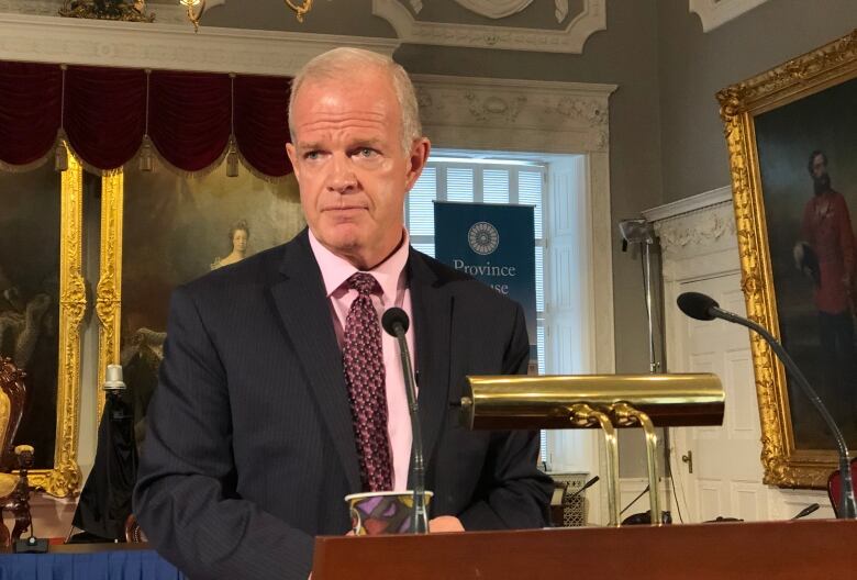 A white man wearing a suit and tie speaks at a podium.